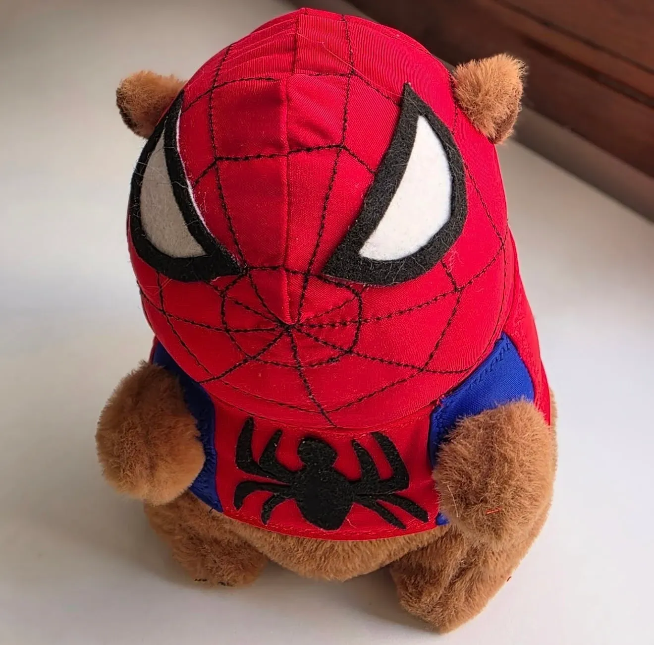 Capibara con capucha roja, telaraña negra, ojos grandes blancos y chaleco rojo y azul