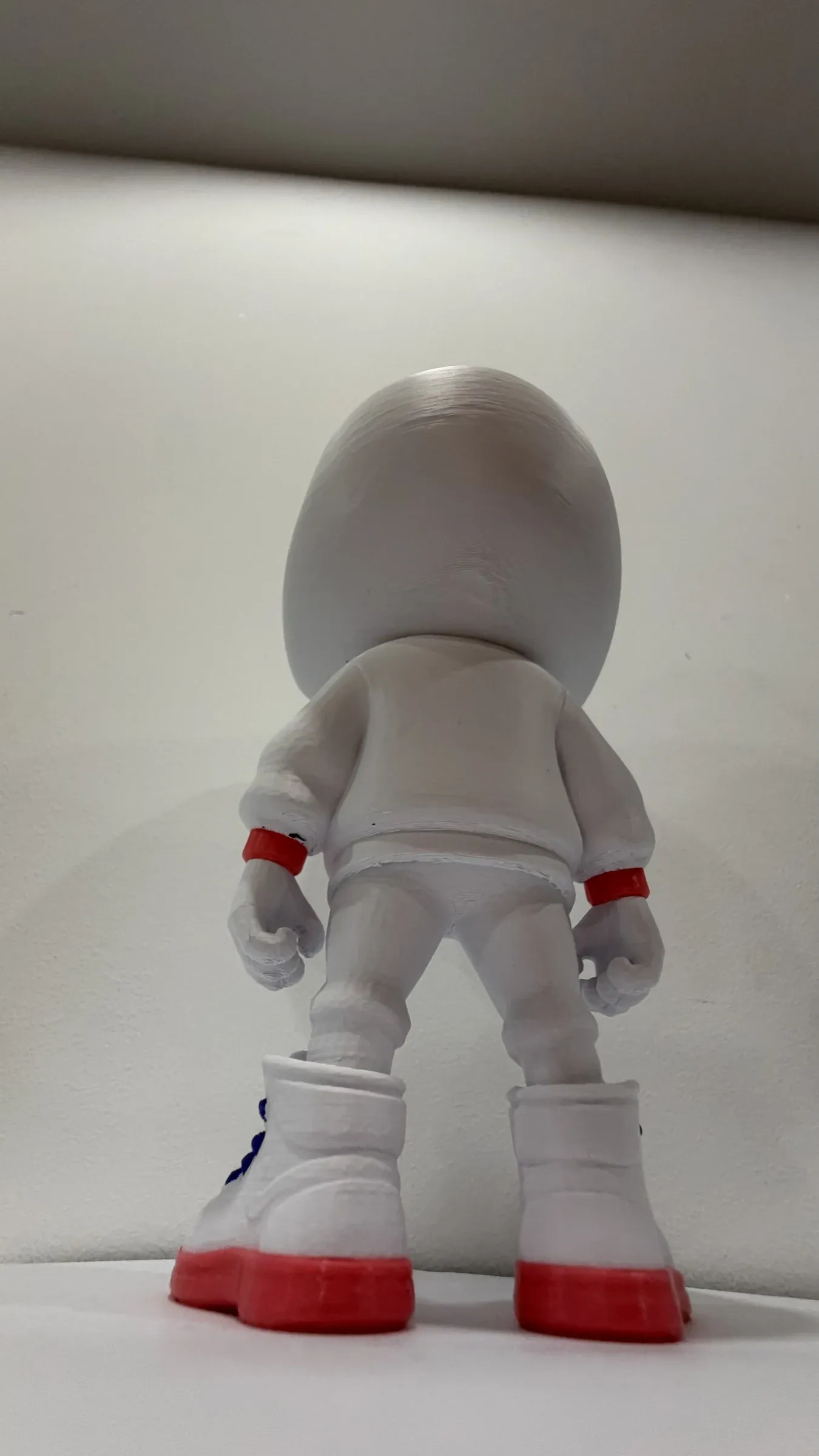 Rear view of the white figure with a large head, red cuffs and tall white boots with red soles.