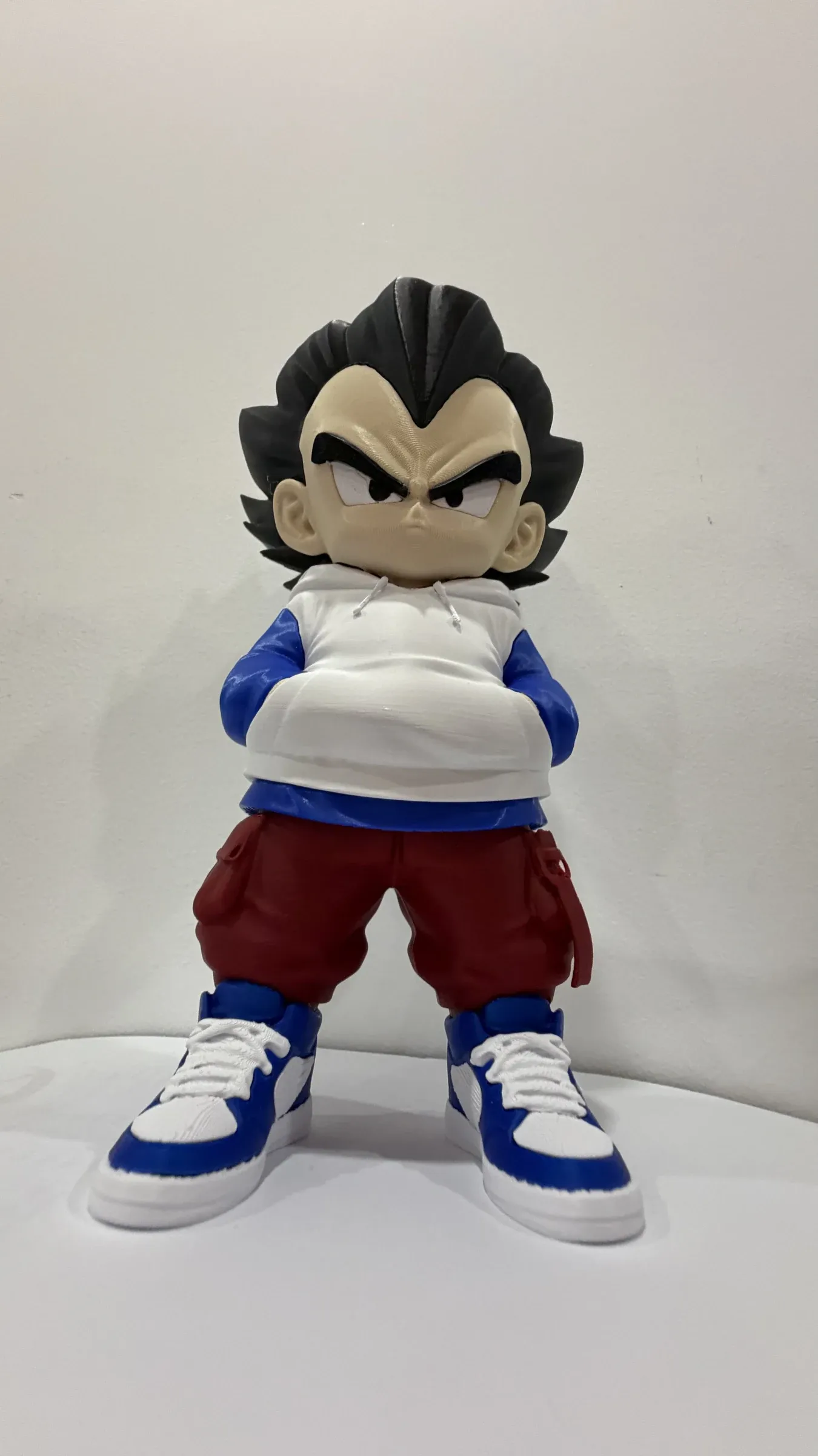 Figure of a boy with spiky black hair, white hoodie, red trousers and arms folded