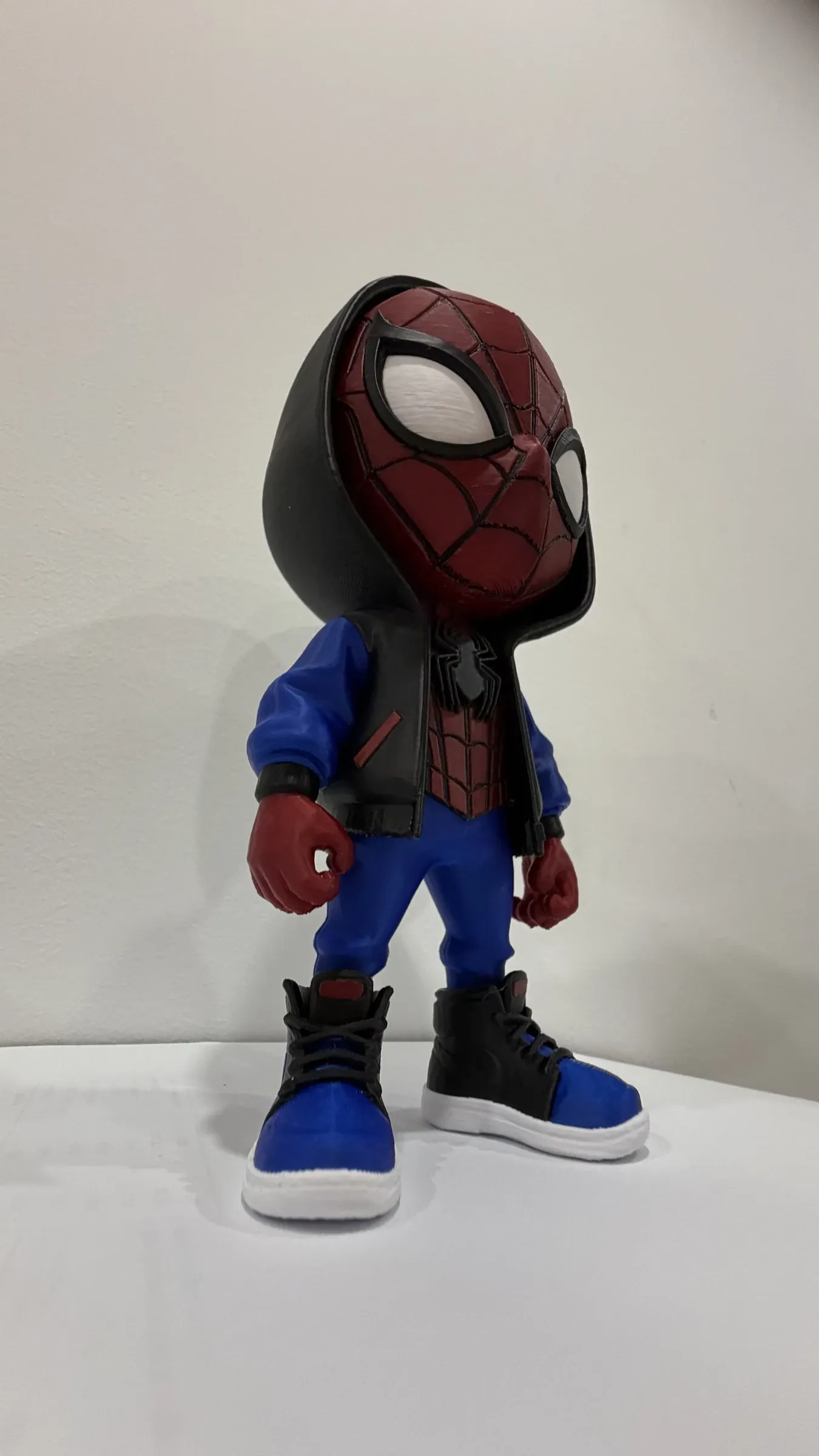 Figura chibi de cabeza grande con máscara roja y telaraña negra, ojos blancos y capucha negra