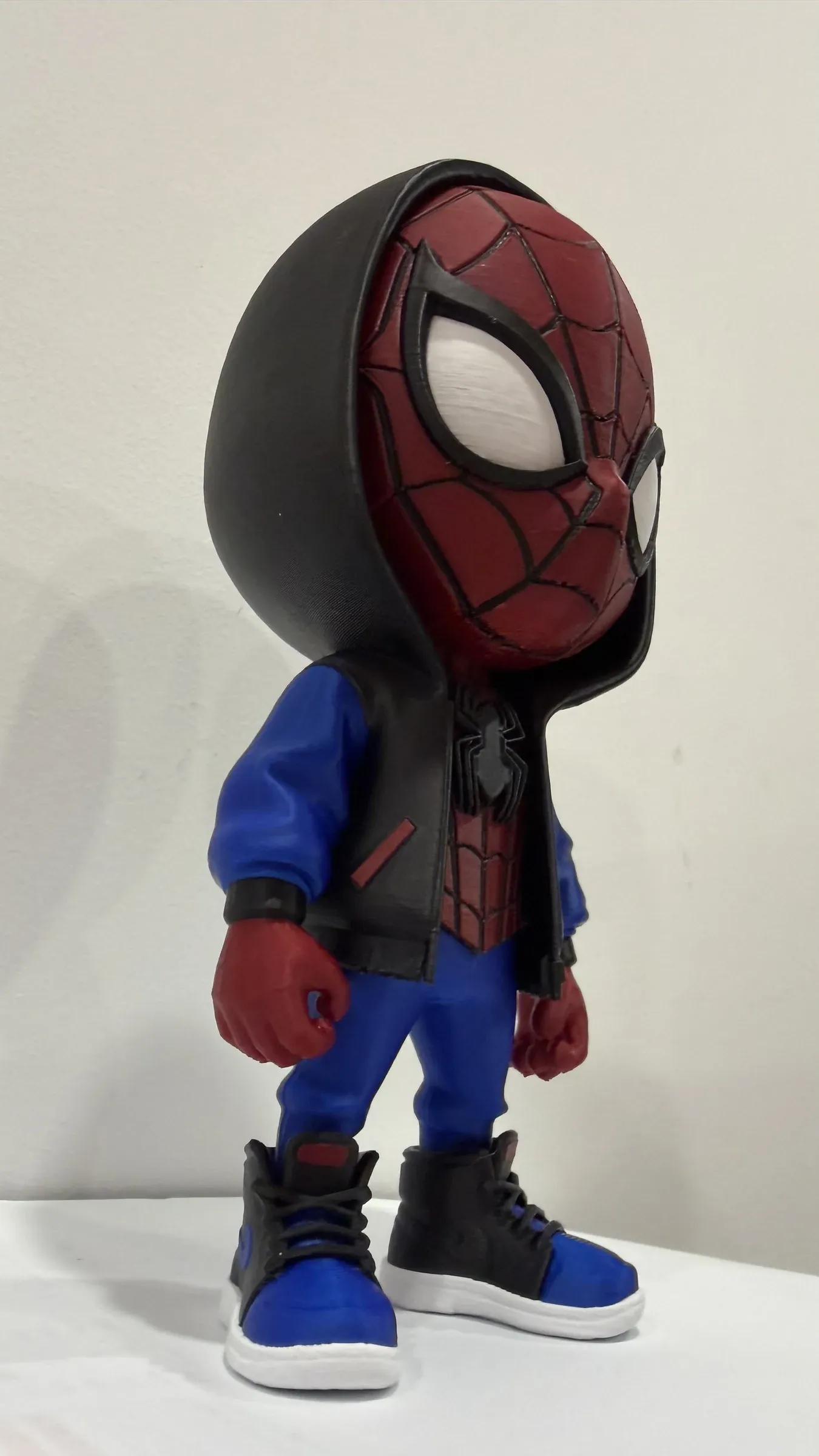 Side view of the chibi figure with black hood, blue jacket and red cuffs on a white surface
