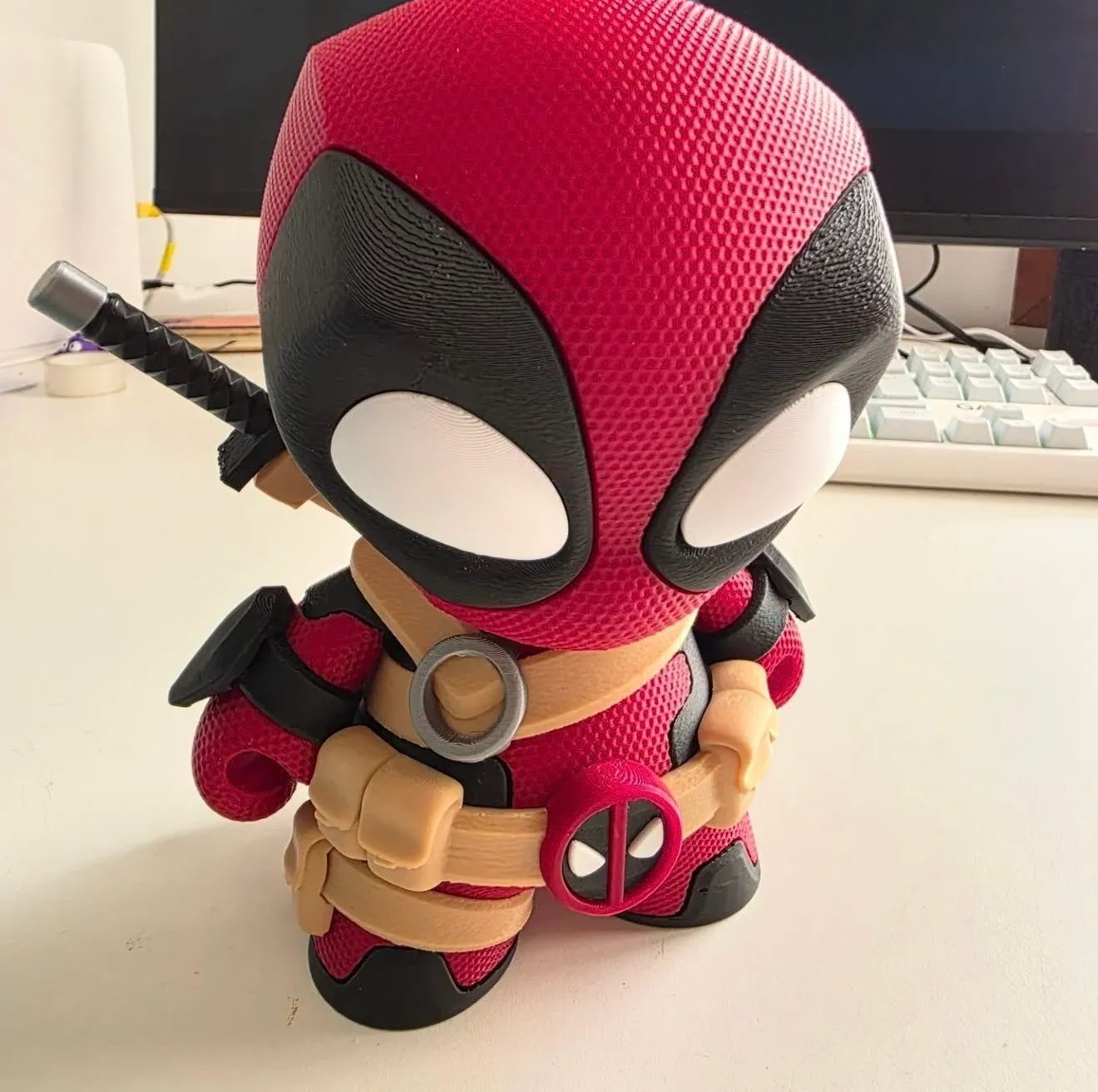 Figura chibi de un mercenario enmascarado con ojos blancos grandes, correas beige y una espada a la espalda, sobre un…
